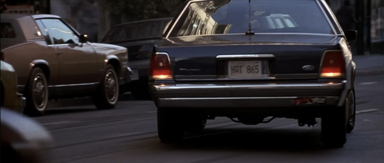 Gang Related (1997) movie still: medium — A city street features several parked automobiles during the day. A dark sedan occupies the foreground…