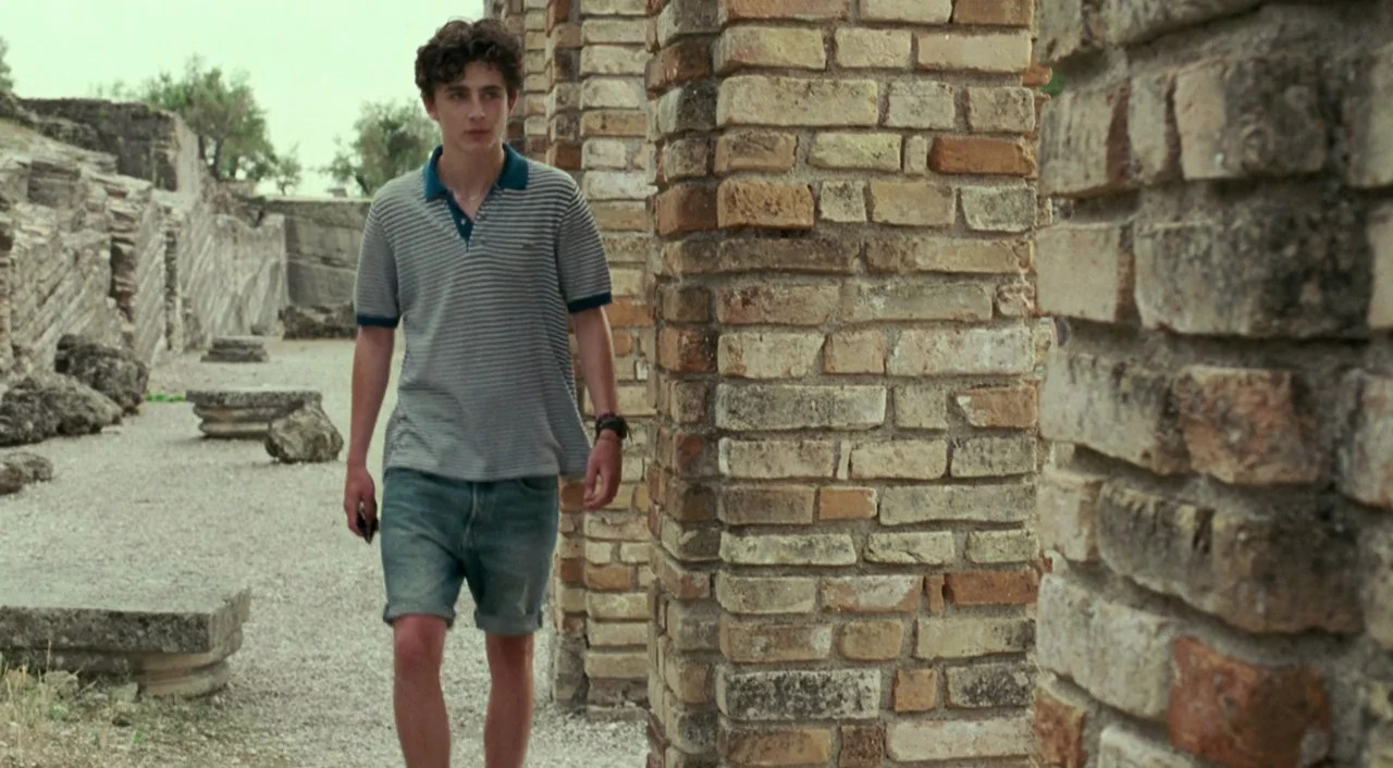 Call Me By Your Name (2017) movie still: fullbody — An archaeological site features large brick pillars arranged in rows with gravel ground. A young…