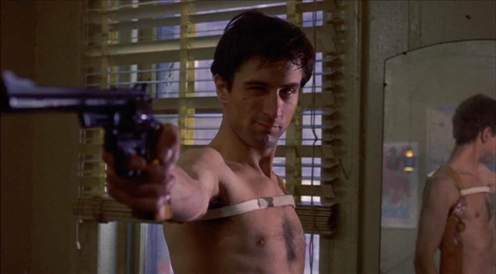 Taxi Driver (1976) movie still: medium — A small residential space featuring a window with venetian blinds and a wall mirror. A shirtless man stands…