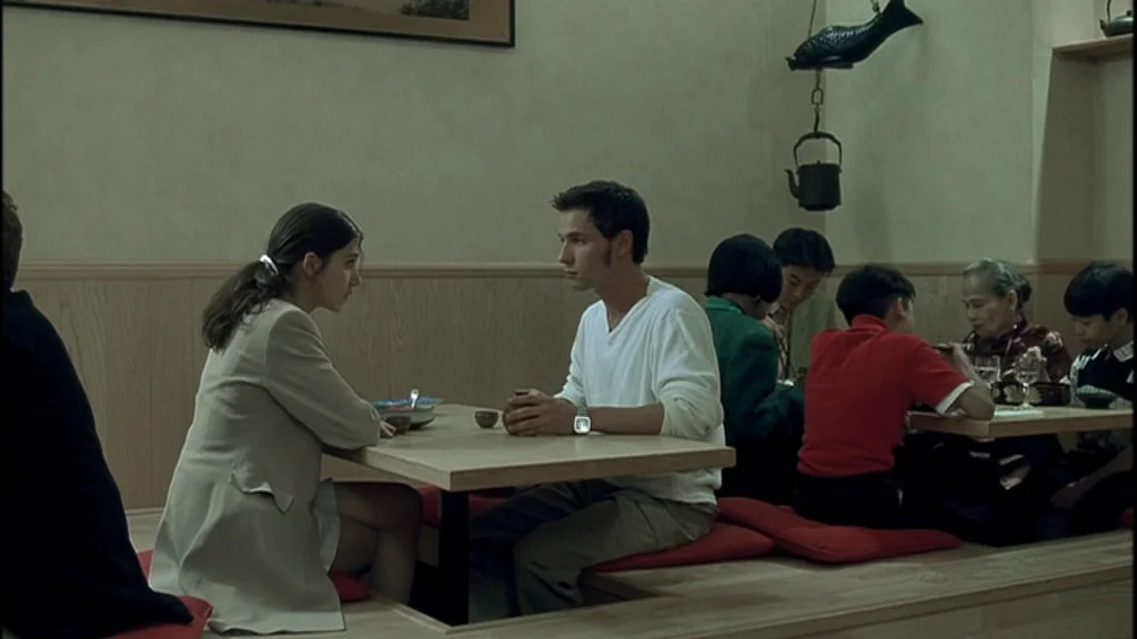 Romance (1999) movie still: medium — A Japanese-style restaurant interior with low wooden tables and red seat cushions. A young couple sits at the…
