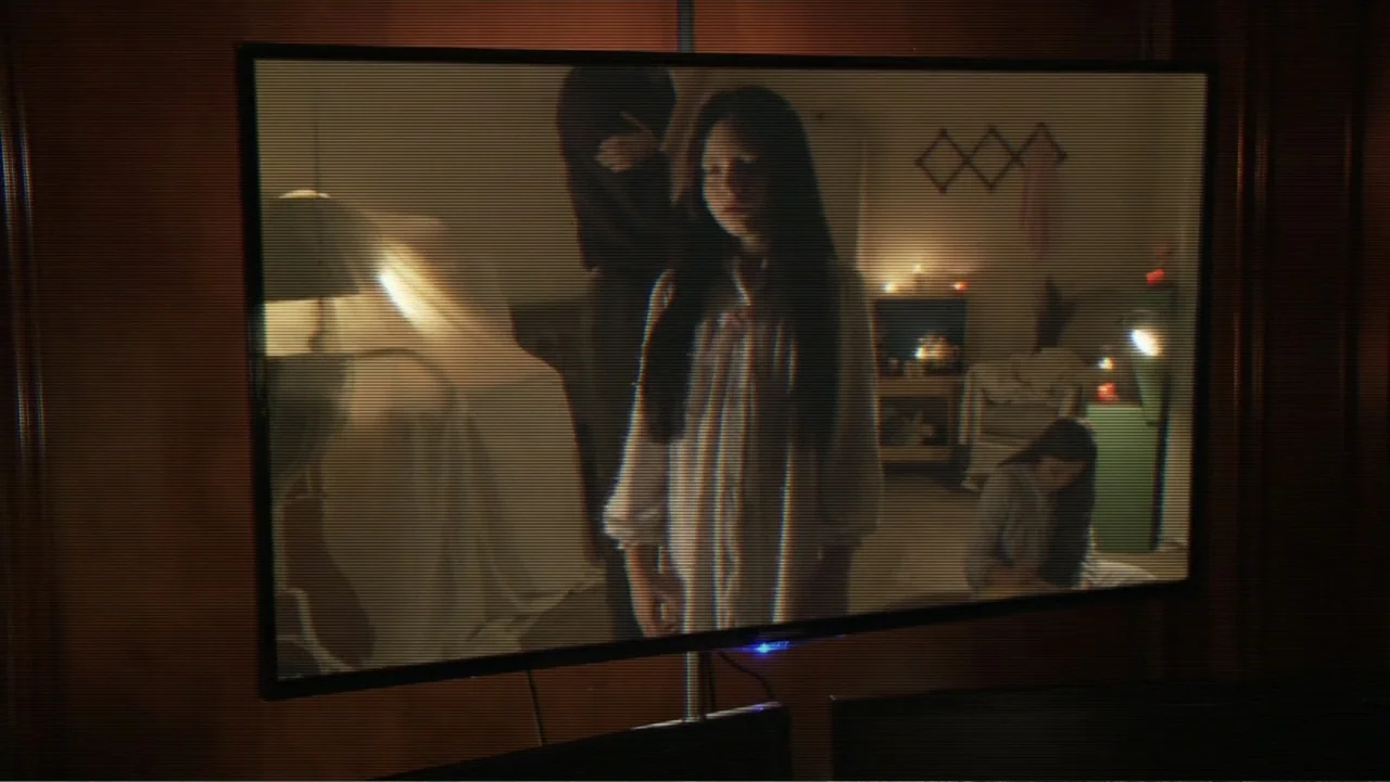 Paranormal Activity: The Ghost Dimension (2015) movie still: medium — A dimly lit room is visible on a flickering television screen at night. A…