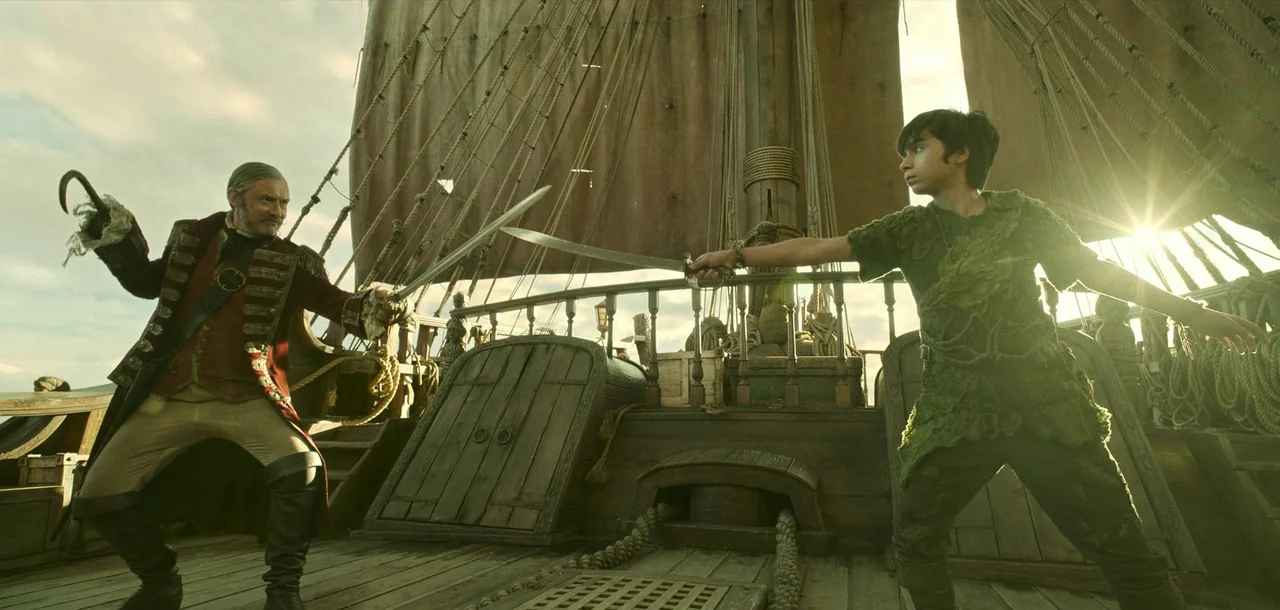 Peter Pan & Wendy (2023) movie still: fullbody — The wooden deck of a sailing ship with ropes and canvas sails visible. A mature man in a red coat…