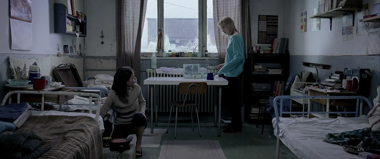 4 months, 3 Weeks and 2 Days (2007) movie still: wide — A cluttered dormitory room contains two metal beds, shelves, and a small dining table. A…