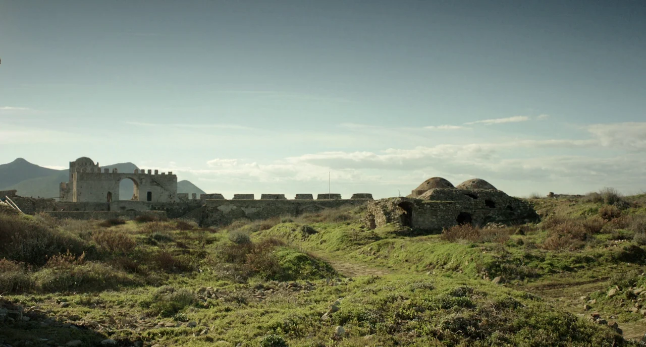 Before Midnight (2013) movie still: establishing — An ancient stone fortress with arched walls stands amidst a rolling green hillside. Domed stone…