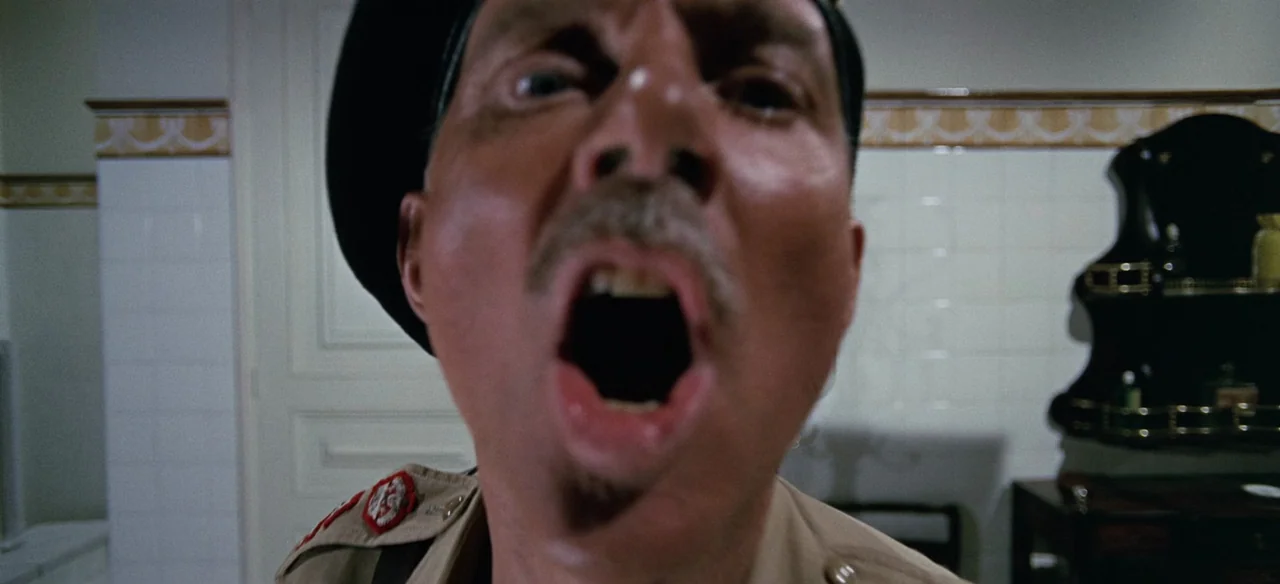 Patton (1970) movie still: closeup — A stark white tiled bathroom features horizontal patterned border trim and a wall-mounted shelf. A middle-aged…