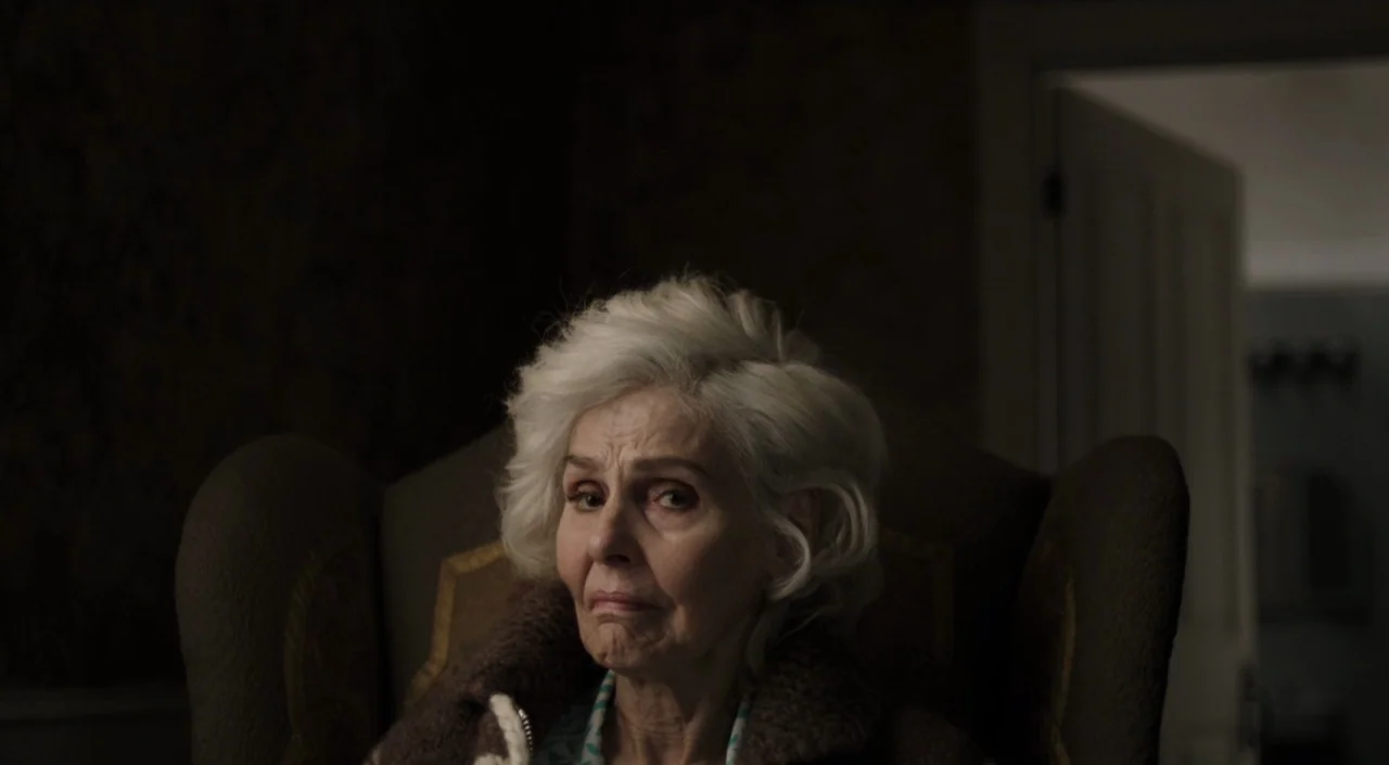 I Am The Pretty Thing That Lives In The House (2016) movie still: closeup — An elderly woman sits in a dark, dimly lit room on a patterned chair.…