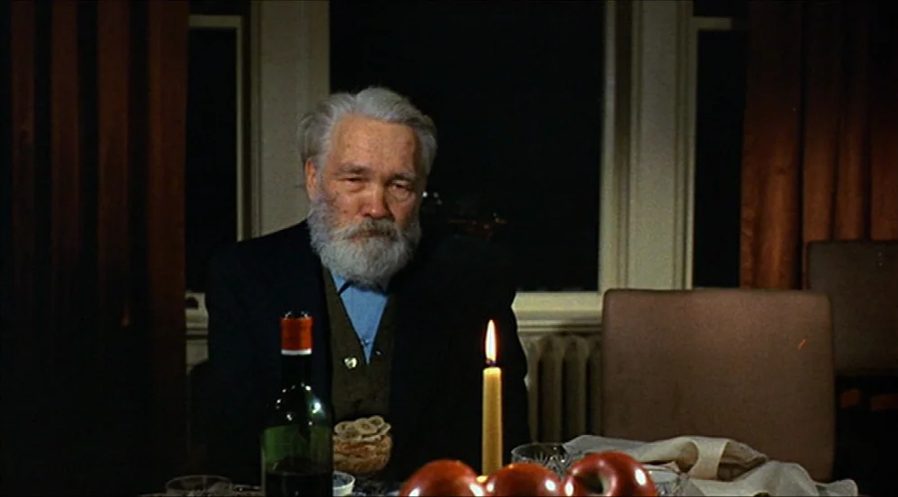 Five Easy Pieces (1970) movie still: medium — A dining table features a burning candle, a wine bottle, and several apples. An elderly man with a…