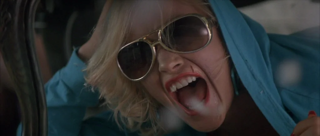 True Romance (1993) movie still: closeup — The interior of a vehicle at night with low, muted lighting conditions. A woman with short blonde hair…