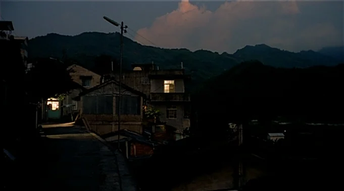 A Summer at Grandpa’s (1984) movie still: establishing — A dark, hilly village landscape features multi-story residential buildings set against a…