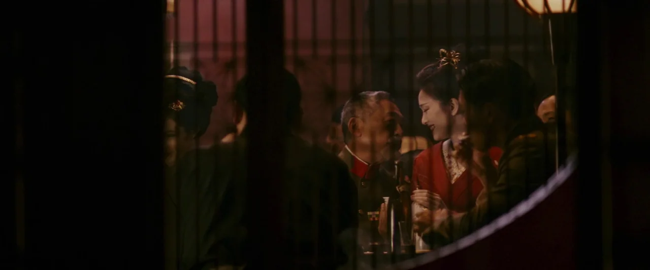 Memoirs of a Geisha (2005) movie still: medium — A dark, wood-paneled establishment viewed through a vertical slat partition at night. An elderly…