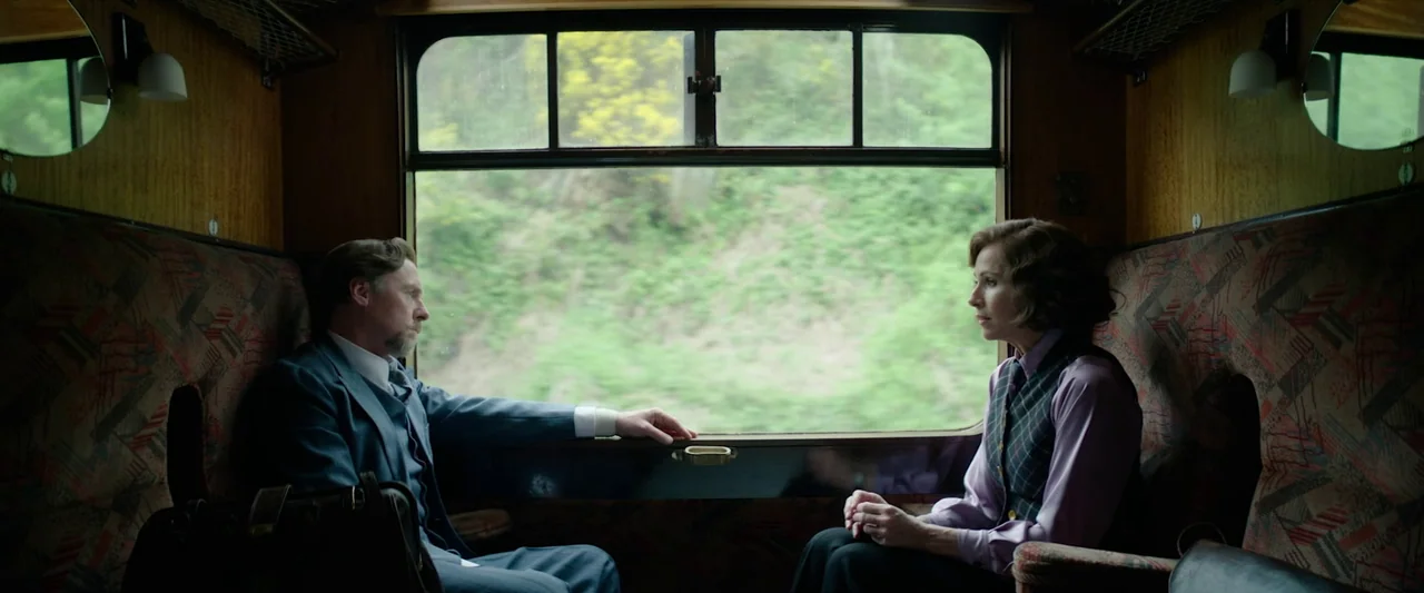 Nandor Fodor and the Talking Mongoose (2023) movie still: medium — A vintage wooden train compartment with patterned seat fabric and a large view…