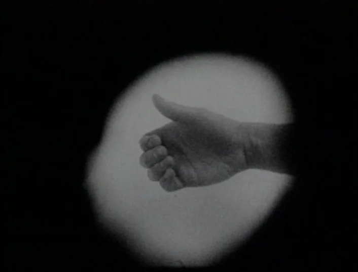 Cowards Bend The Knee (2003) movie still: closeup — An abstract dark void centers on a brightly lit hand. The hand is positioned as if reaching…