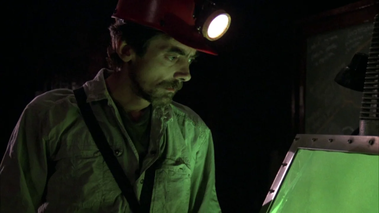 Day of the Dead (1985) movie still: medium — A dark, dimly lit environment features industrial equipment with a glowing green monitor. A man wearing…