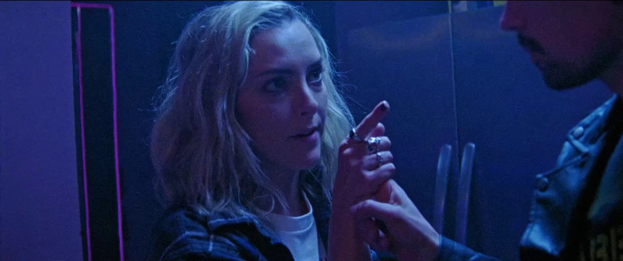 Christmas Bloody Christmas (2022) movie still: medium — A dark kitchen interior is illuminated by a cold blue neon glow from off-screen. A blonde…