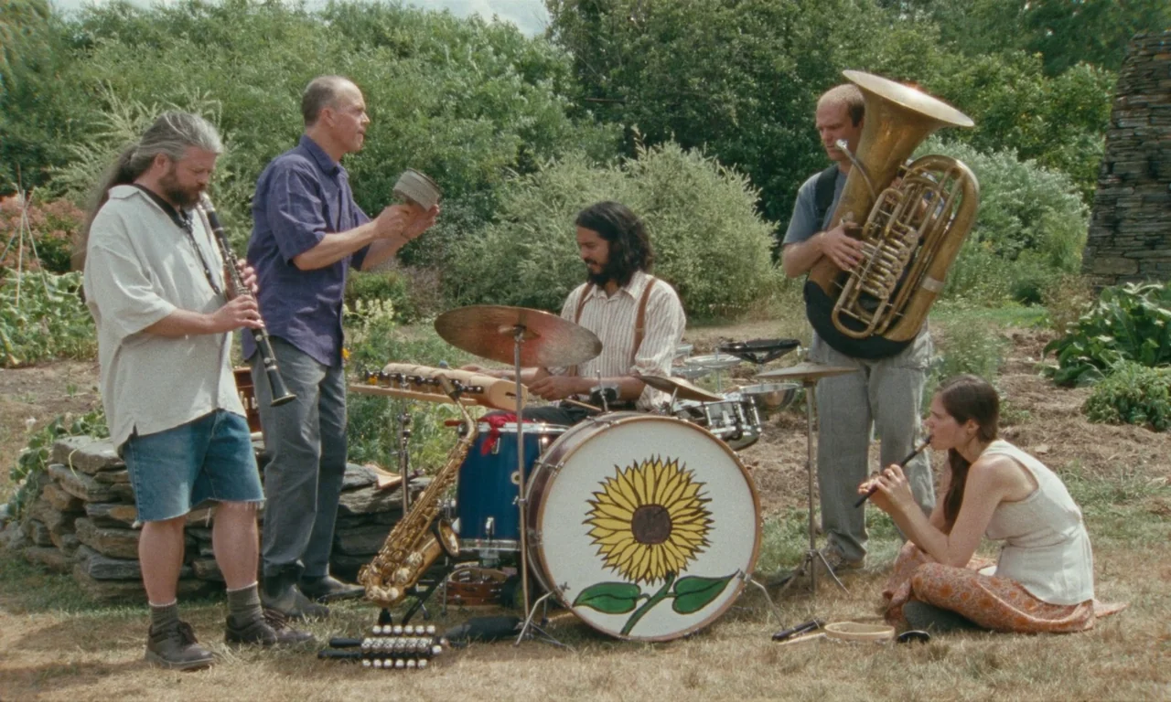 Janet Planet (2023) movie still: wide — A group of musicians performs in an outdoor patch with stacked stone walls. A drummer sits behind a…