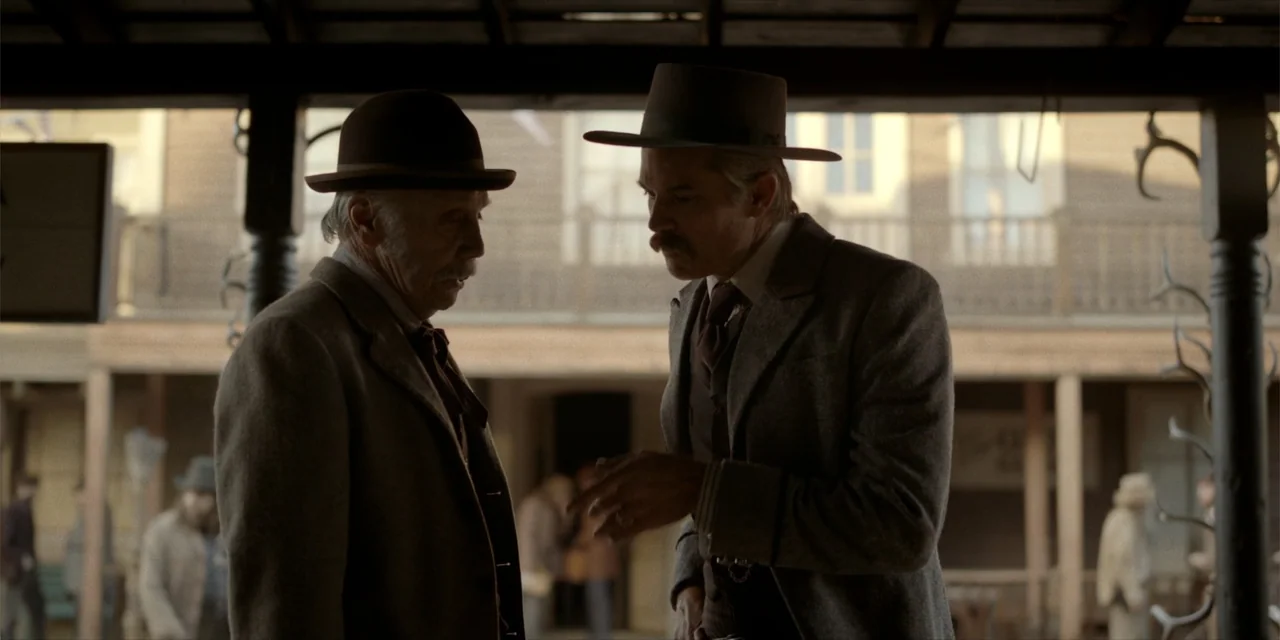 Deadwood: The Movie (2019) movie still: medium — A wooden covered walkway lines a dusty street in a historical western frontier town. Two men in…