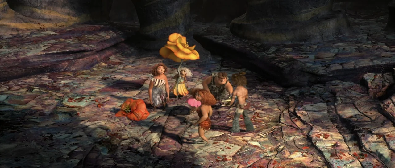 The Croods (2013) movie still: fullbody — A rocky, uneven terrain is covered in scattered orange and pink prehistoric flowers. A small group of…