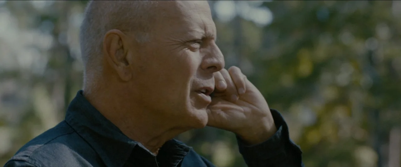 Ambush (2020) movie still: closeup — An outdoor area with blurred green foliage in the background under natural daylight. A mature man in a dark…