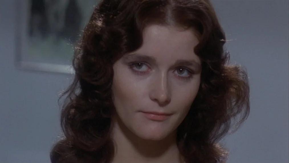 Sisters (1973) movie still: closeup — A plain grey room serves as the setting for the subject. A woman looks forward while her brown wavy hair…