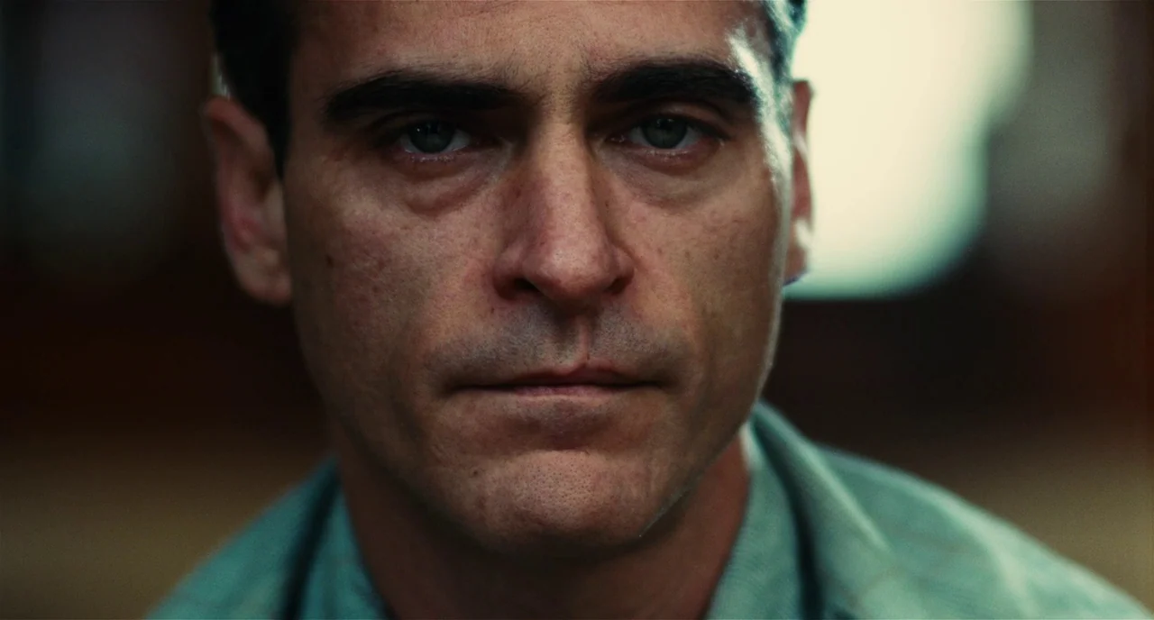 The Master (2012) movie still: closeup — A close-up shot focuses on a man in a simple interior setting. The man faces forward while light from a…
