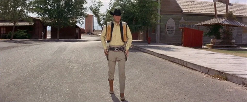 Viva Las Vegas (1964) movie still: fullbody — An unpaved street in a western town with wooden buildings flanking both sides. A man in western attire…