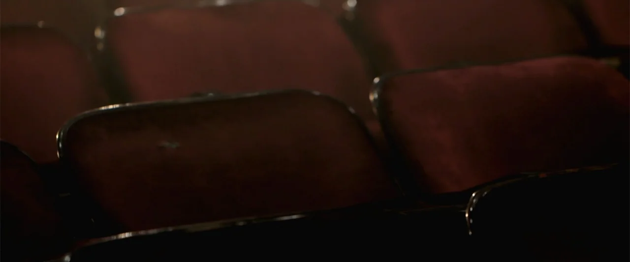 Maxine's Baby: The Tyler Perry Story (2023) movie still: closeup — A row of dark red velvet movie theater seats fills the dark frame. The chairs are…