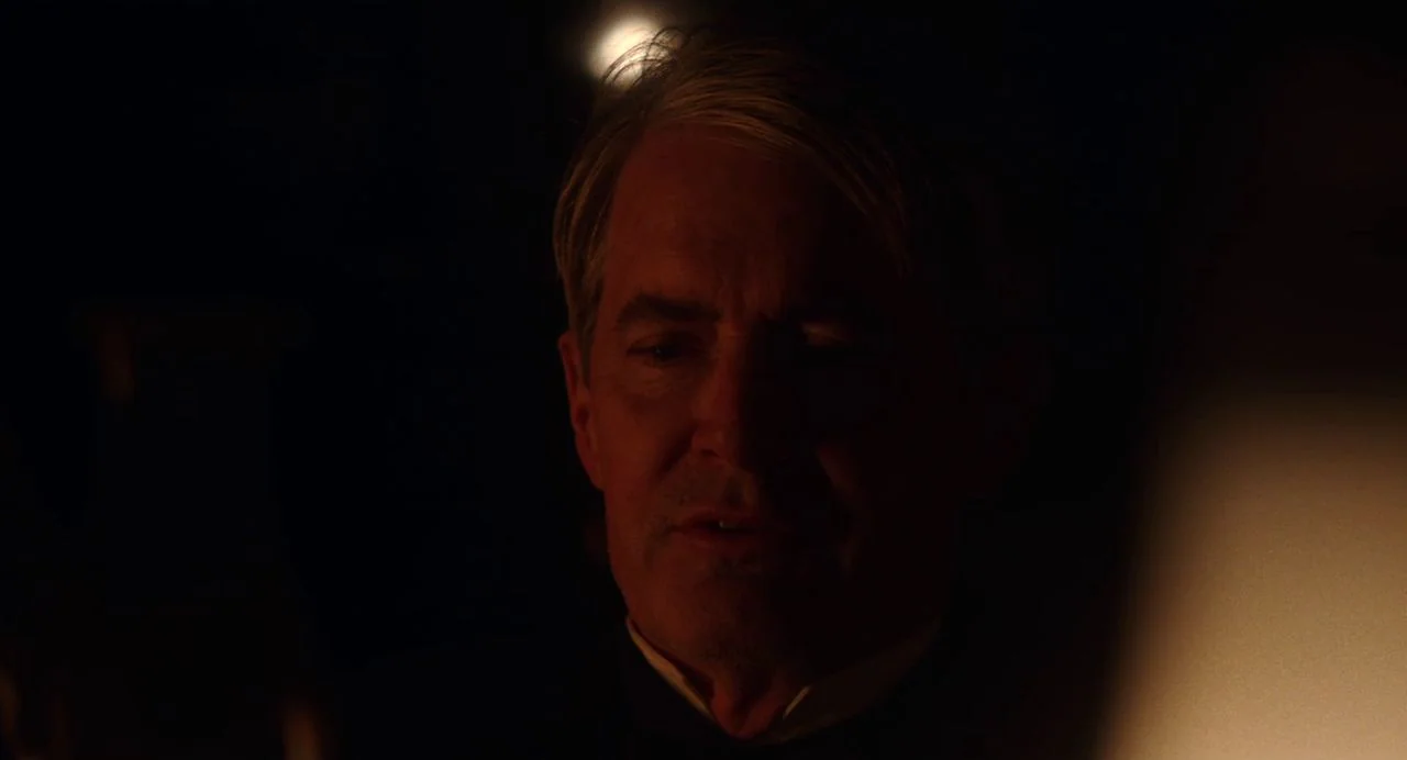 Tesla (2020) movie still: closeup — A man stands in a dark environment with a single bright light source present. The subject is partially…