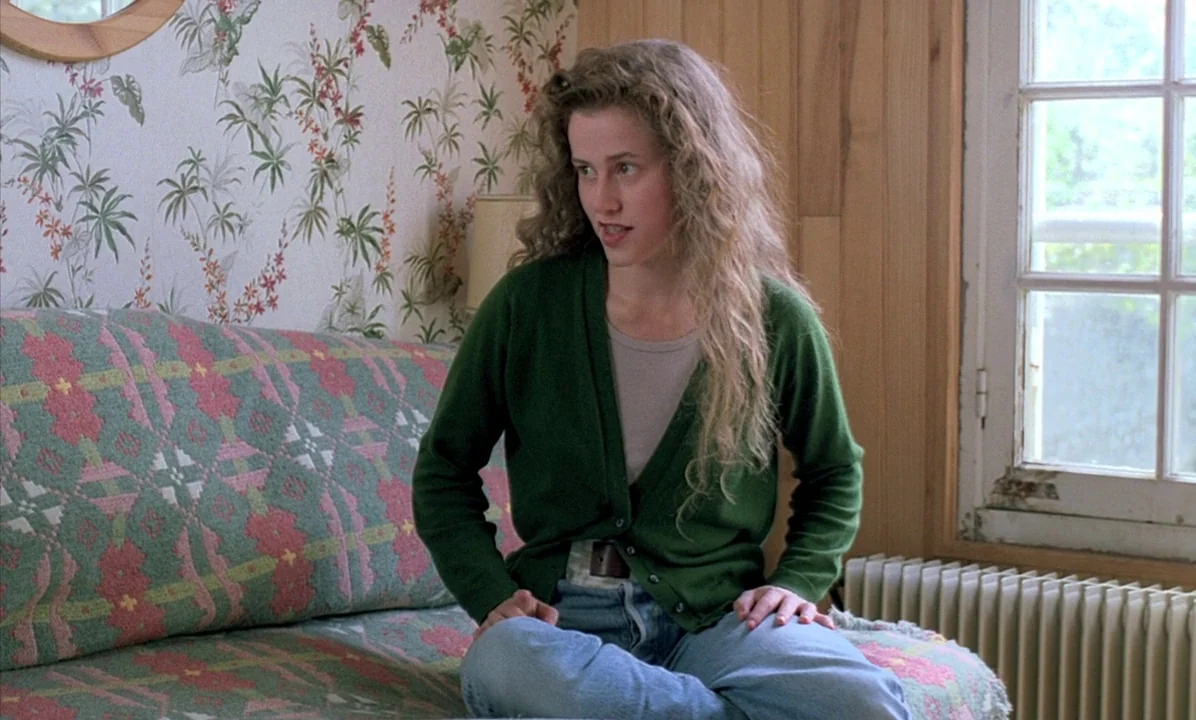 A Tale of Springtime (1990) movie still: medium — A domestic space features floral wallpaper and wood paneling behind a patterned sofa. A young…