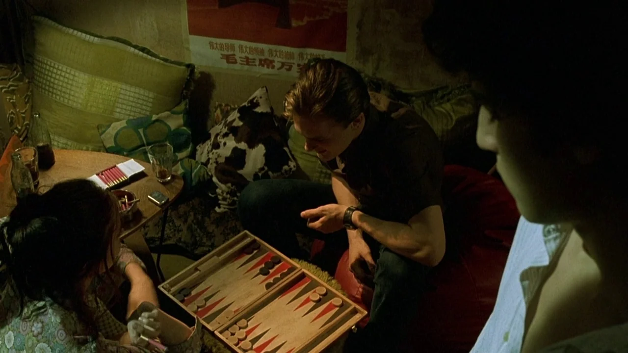 The Dreamers (2003) movie still: medium — A cramped room filled with floor pillows and a vintage Chinese political propaganda poster. A man and a…
