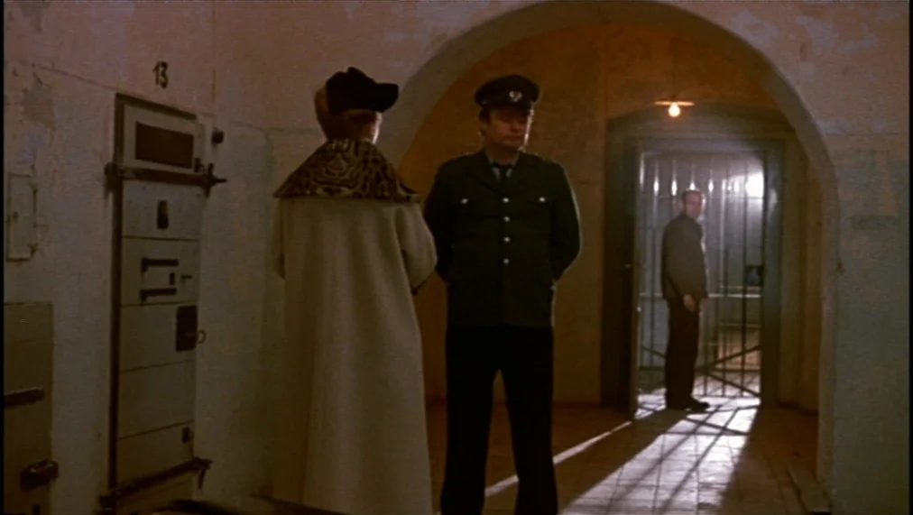 The Marriage of Maria Braun (1979) movie still: fullbody — A stone prison corridor with an arched doorway and peeling paint on walls. A uniformed…
