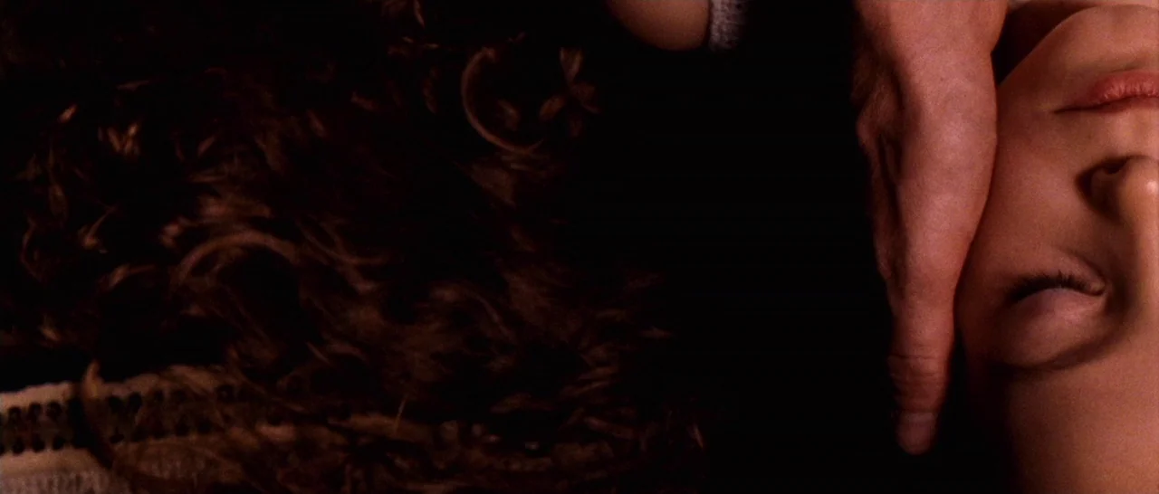 Amer (2009) movie still: closeup — A dark bedroom interior at night features a person resting in bed. A hand gently touches the side of her face in…