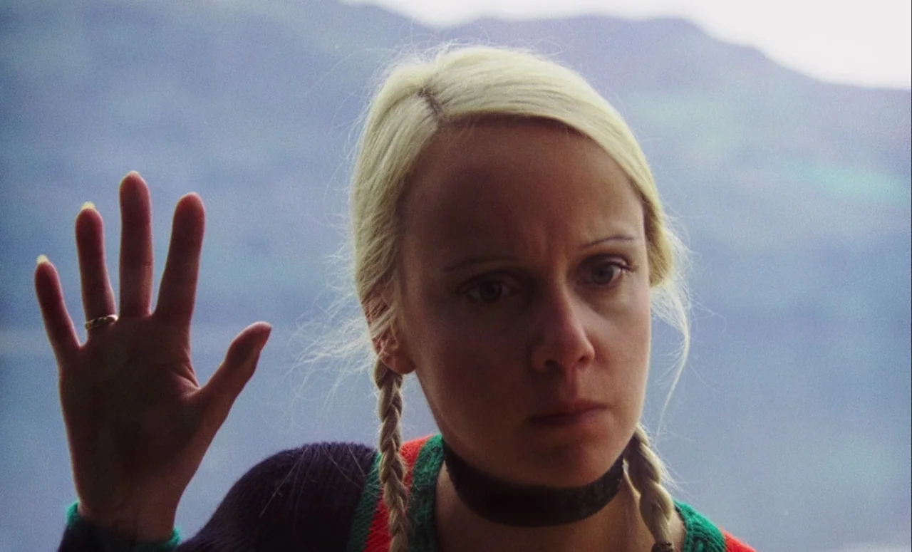 Mahler (1974) movie still: closeup — A woman stands in front of a blurry, mountainous landscape. She presses her palm flat against a transparent…