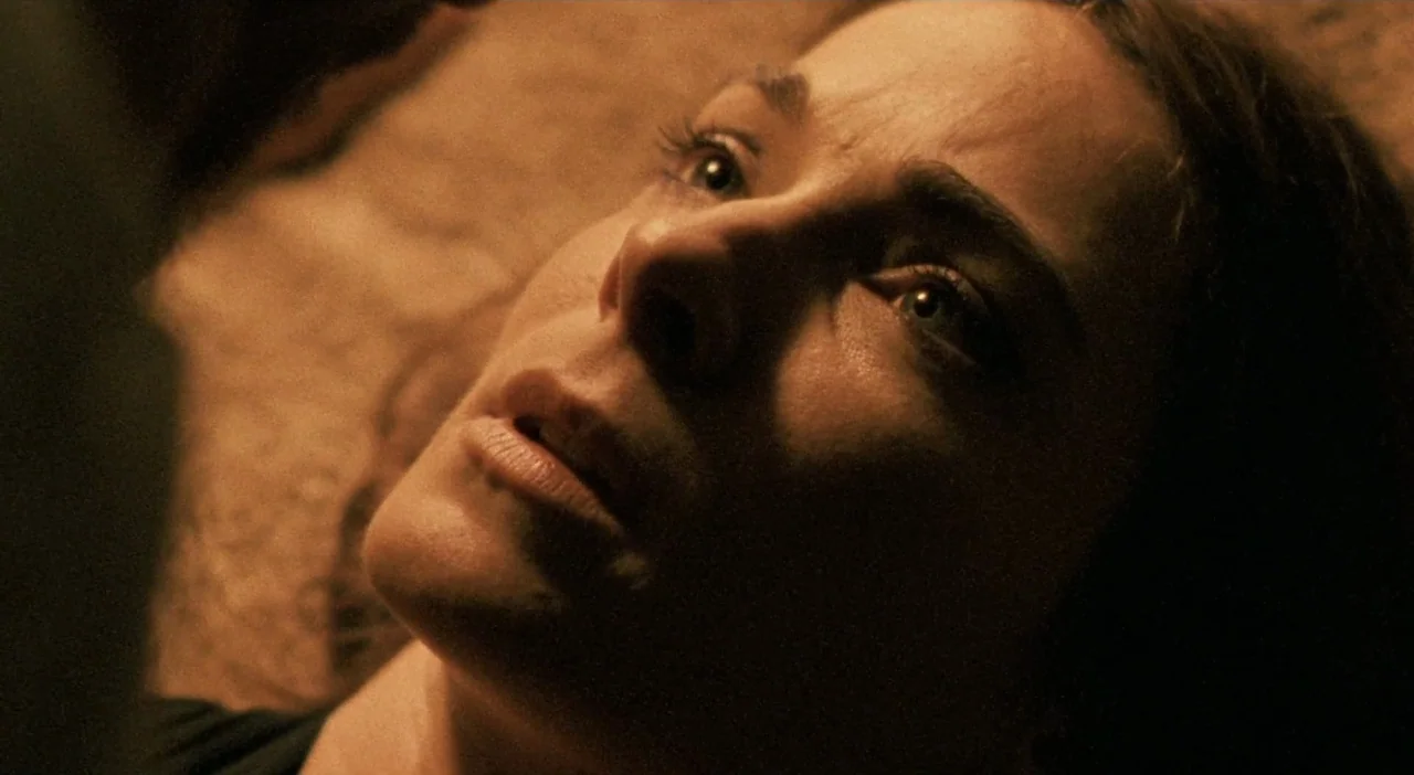 Patagonia (2010) movie still: closeup — A dimly lit room with warm amber light cast upon a woman's face. The woman lies horizontally in the frame…