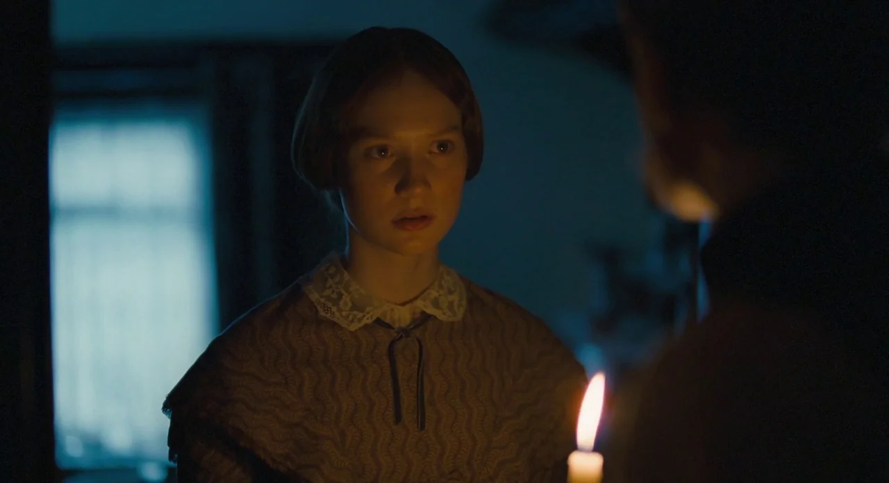 Jane Eyre (2011) movie still: medium — A dim room at night shows a woman illuminated by candlelight. She faces a person positioned in the foreground…