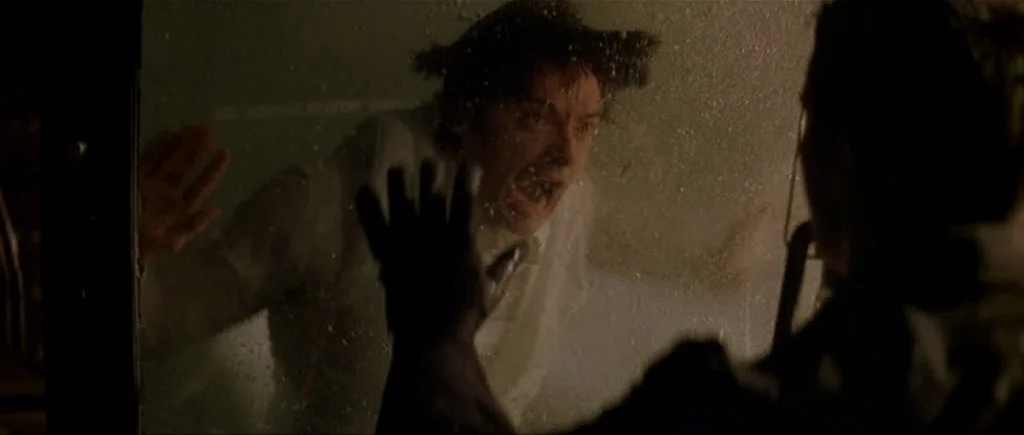 The Prestige (2006) movie still: medium — A dim train car at night features a man looking through a glass pane. The man holds his palms flat against…
