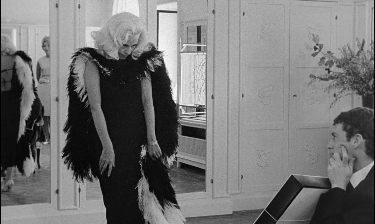 Bay of Angels (1963) movie still: medium — A light-toned room features tall mirrors with ornate paneling on the surrounding walls. A woman in a dark…