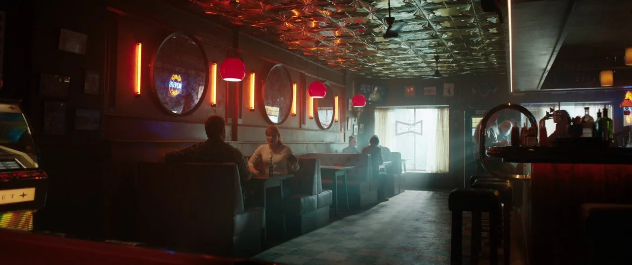 Jurassic World: Fallen Kingdom (2018) movie still: wide — A dimly lit bar features a metallic ceiling grid and dark wood-paneled walls. A man and…