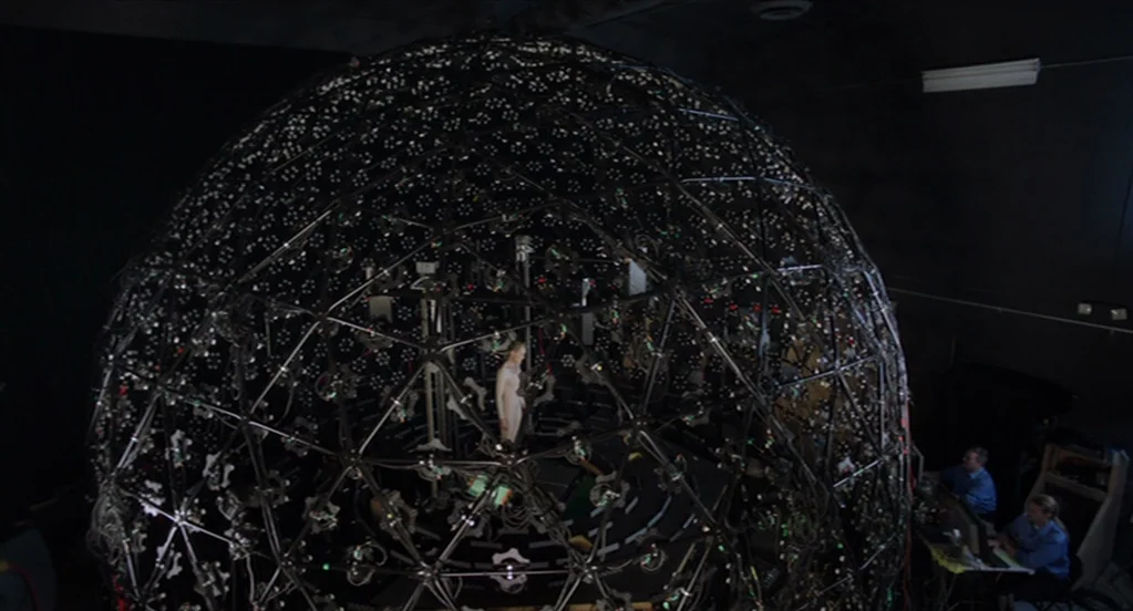 The Congress (2013) movie still: wide — A large spherical rig made of interconnected metal struts and numerous camera lenses surrounds a subject. A…