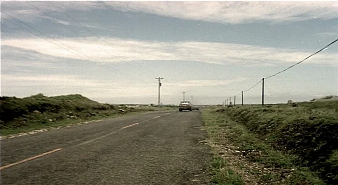 The Boys From Fengkuei (1983) movie still: establishing — A long stretch of asphalt road cuts through a desolate, grassy rural landscape. A lone…