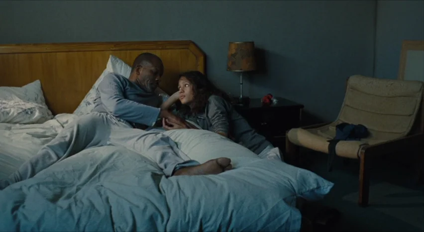 35 Shots of Rum (2008) movie still: medium — A spartan bedroom features a wooden headboard against a plain grey wall. A man and a woman lie together…