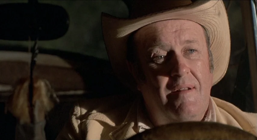 Blood Simple (1984) movie still: closeup — A man drives a vehicle at night with dim interior illumination. The cowboy hat shades part of his face as…