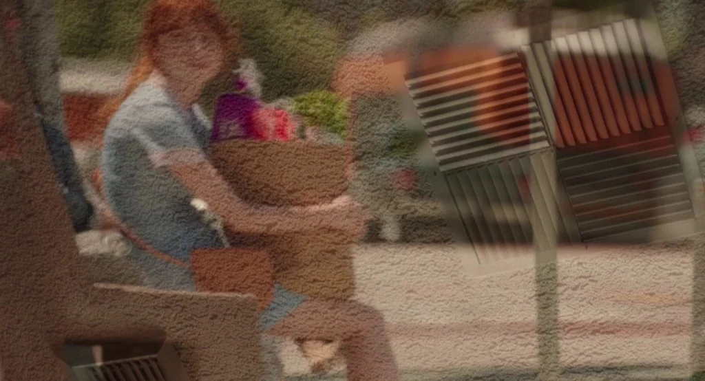 Ruby Sparks (2012) movie still: medium — A woman sits on a bench on a paved surface. She holds a paper grocery bag in her lap.