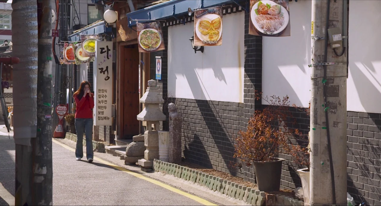 Nobody’s Daughter Haewon (2013) movie still: wide — A narrow paved alleyway in South Korea features a white wall with dark brick. A young woman…