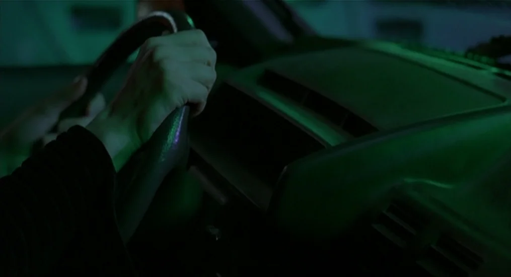 Vendredi Soir (2002) movie still: closeup — The dark interior of a car features a plastic dashboard and steering wheel. A person's hand firmly grips…