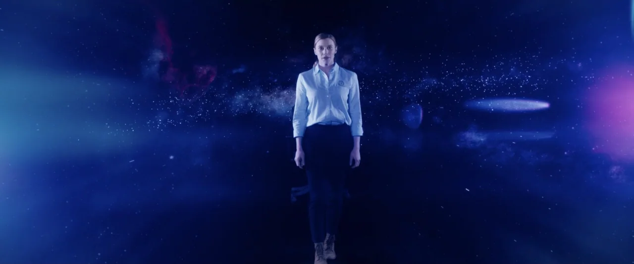 2036 Origin Unknown (2018) movie still: fullbody — A woman stands centered against a deep space background filled with distant nebulae stars. She…