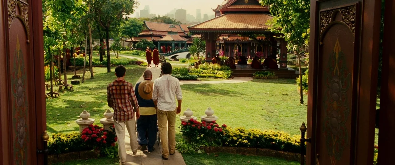 The Hangover Part II (2011) movie still: wide — A green lawn contains a traditional Thai-style temple building with red roof tiles. Three men walk…