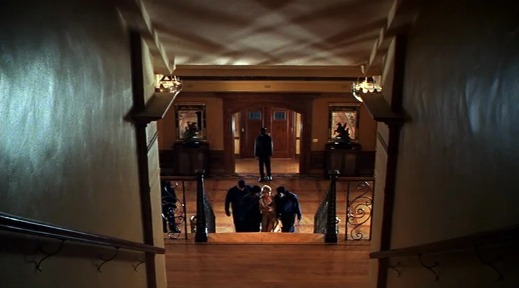 Out Of Sight (1998) movie still: wide — A spacious mansion foyer with hardwood flooring and an ornate wooden staircase. Several individuals in…