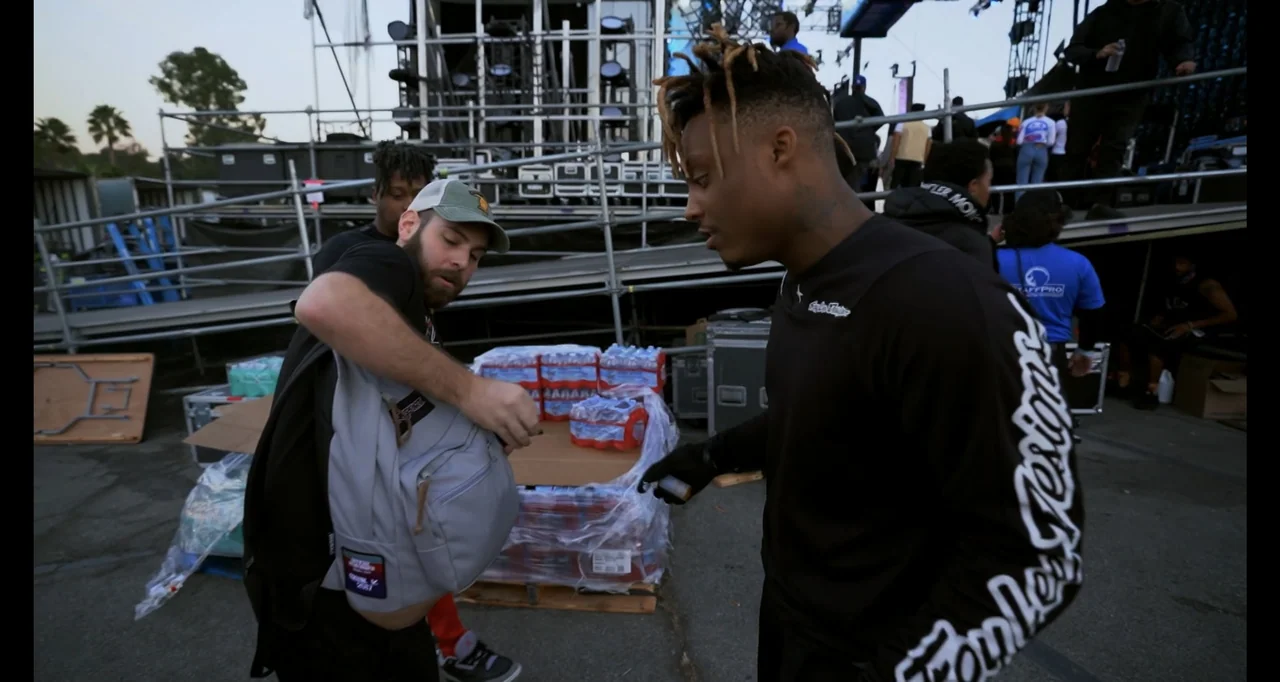 Juice WRLD: Into the Abyss (2021) movie still: medium — A festival backstage area features metal scaffolding and pallets of stacked water bottles. A…