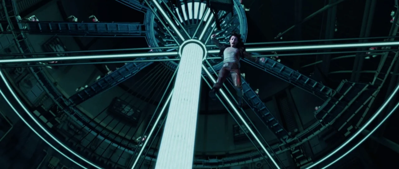 I, Robot (2004) movie still: wide — A dark, complex industrial interior with a massive circular light structure spanning the ceiling. A woman is…