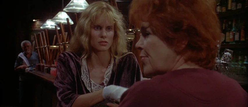Short Cuts (1993) movie still: medium — A dimly lit bar with stools stacked on the counter in the background. A blonde woman speaks to a woman with…